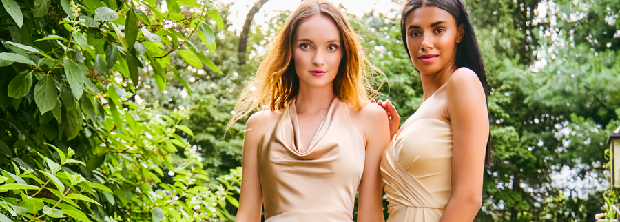 Two women in beige dresses standing on stone steps with greenery in the background