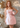 Woman in a pink dress standing in front of a 'Let's Party' backdrop with balloons.